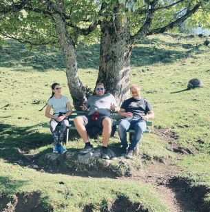 Drei Personen der Reisegruppe sitzend auf einer Bank unter einem Baum in einer Almwiese